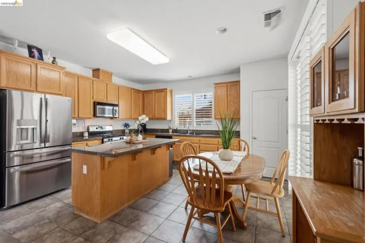 Kitchen featuring a central island with countertop seating, stainless steel appliances, abundant cabinetry, tiled flooring, and window shutters