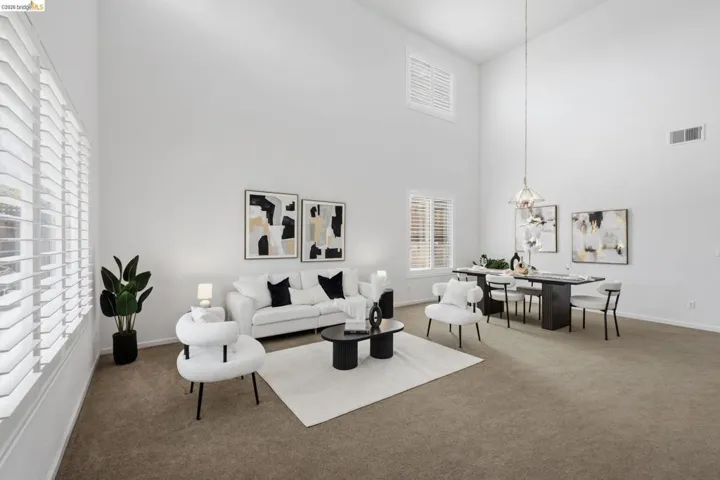 Expansive living area featuring soaring vaulted ceilings, multiple windows with white plantation shutters, and recessed lighting