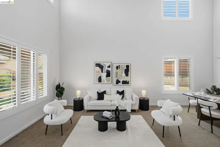 Vaulted ceiling living space featuring multiple windows with white plantation shutters, neutral-toned carpeting, and an open-concept dining area
