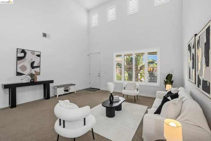Living area featuring vaulted ceilings, a prominent front entry door, and large window installations with privacy shutters