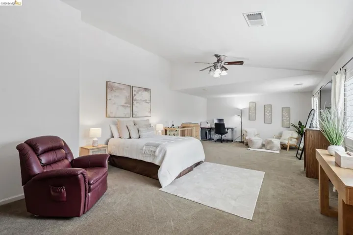 Spacious room featuring vaulted ceilings, a ceiling fan with light, plush carpet flooring, and window blinds