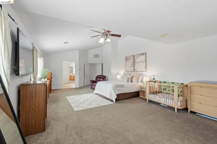 Spacious bedroom featuring vaulted ceilings, carpet flooring, a ceiling fan with integrated lighting, and multiple windows providing natural light