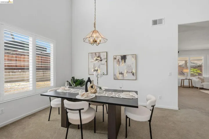 Dining space featuring a vaulted ceiling with a hanging chandelier, white plantation shutters, and light-toned carpeting