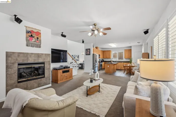 Open-concept living space featuring a tile-surround fireplace, a ceiling fan, and carpet flooring