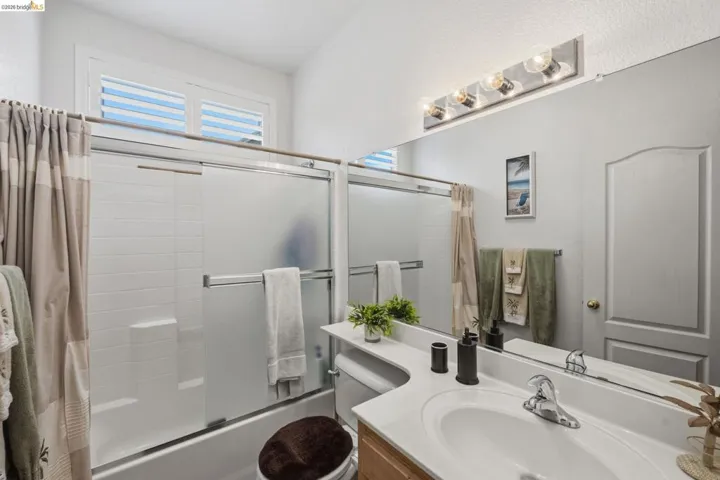 Bathroom featuring a combined tub and shower with sliding glass doors, a white tile surround, a built-in vanity with a white countertop and integrated sink, a wall-mounted mirror, and overhead lighting