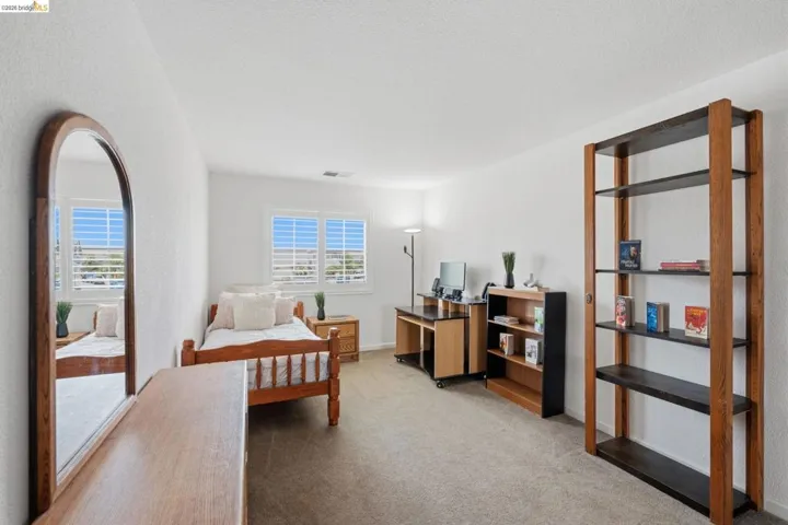 Carpeted room with white walls and a pair of windows featuring white plantation shutters