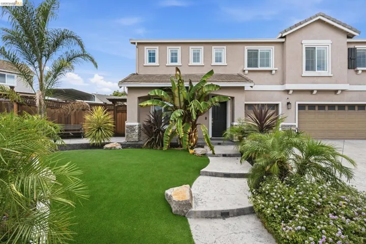 Stucco exterior with stone accents, a concrete pathway, a manicured lawn, an integrated two-car garage, and established landscaping