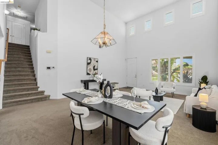 Two-story living area with vaulted ceilings, large windows with plantation shutters, a prominent staircase with carpeted treads and wood railings, and a decorative chandelier