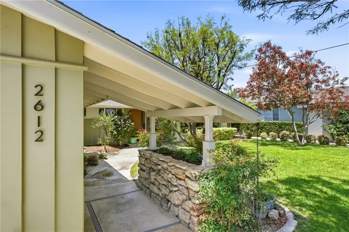The mid-century character is retained in this covered walkway with stone planter, vertical wood garage door, and board and baton house siding.