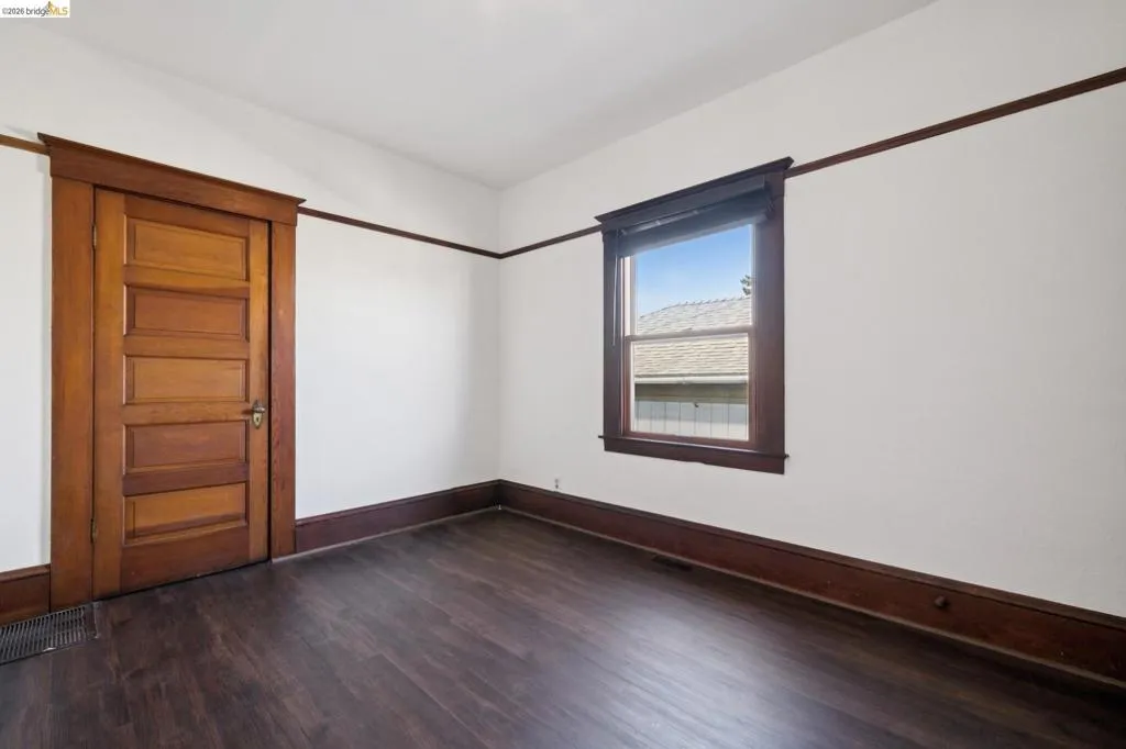 Interior room featuring a wood-finish floor, white walls, and dark wood trim