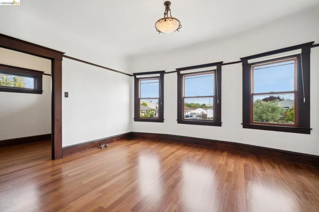 Bright interior space featuring wood-finish flooring, dark wood trim, multiple windows, a ceiling-mounted light fixture, and an open doorway
