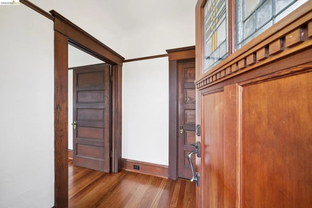 Entryway featuring a rich wood-finish door with leaded glass transom, complemented by wide wood-finish trim and wood-finish flooring
