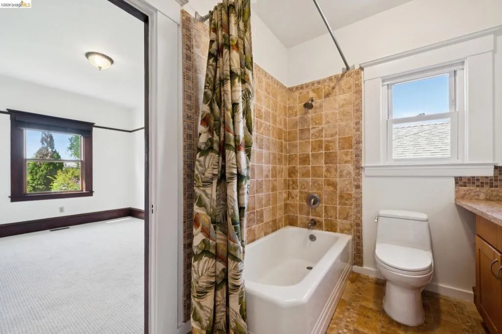Bathroom featuring a tiled tub surround, white bathtub, and single-pane window