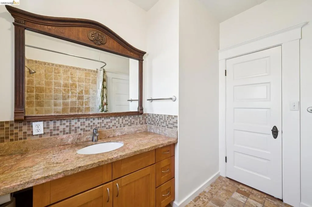 Bathroom with a wood-finish vanity, light-toned countertop, and mosaic tile backsplash