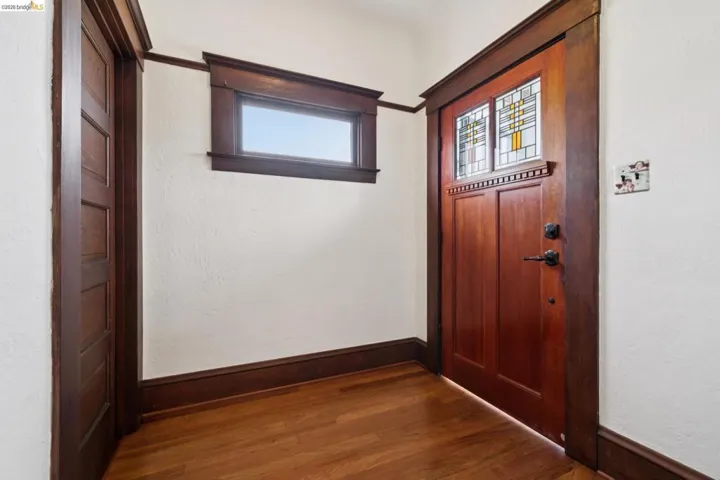 Entryway featuring a rich wood-paneled door with stained glass accents, hardwood flooring, detailed wood trim, and a high transom window