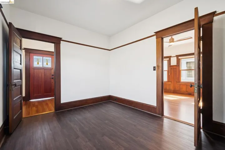 Room featuring dark wood-finish flooring, white walls with dark wood trim, and two doorways with solid wood doors
