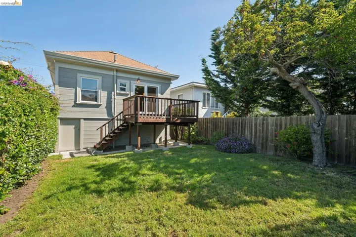 Expansive backyard featuring a manicured lawn, a large wood deck with stairs, a mature tree, and a tall privacy fence