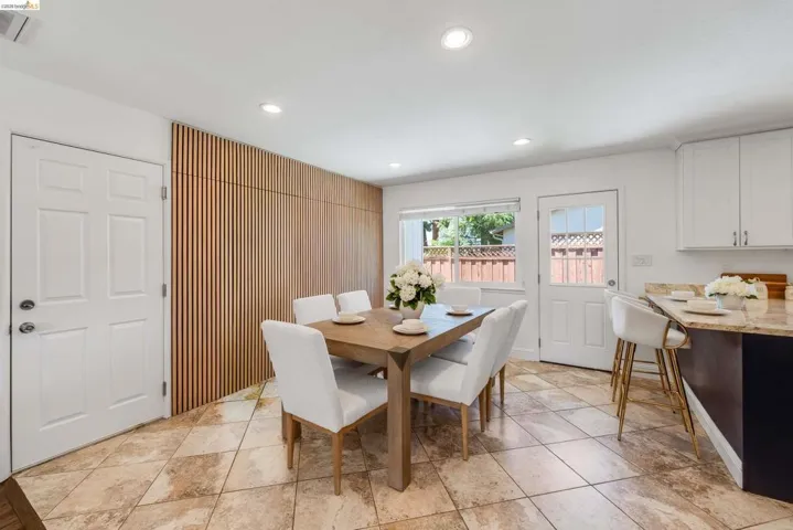 Contemporary dining area featuring a wood-slat accent wall, recessed lighting, and large format floor tiles
