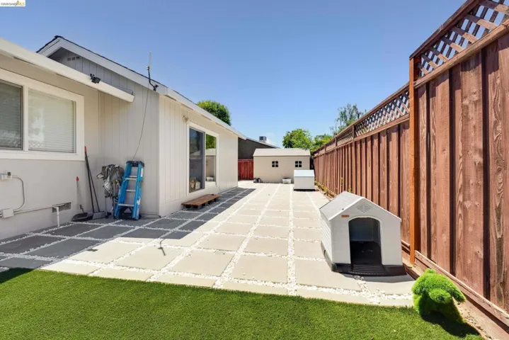 Backyard featuring artificial turf, a paver patio with gravel accents, and a tall wood privacy fence with lattice detailing