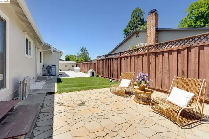 Flagstone patio featuring a full privacy fence with lattice top, a manicured lawn, and a secondary paved patio area