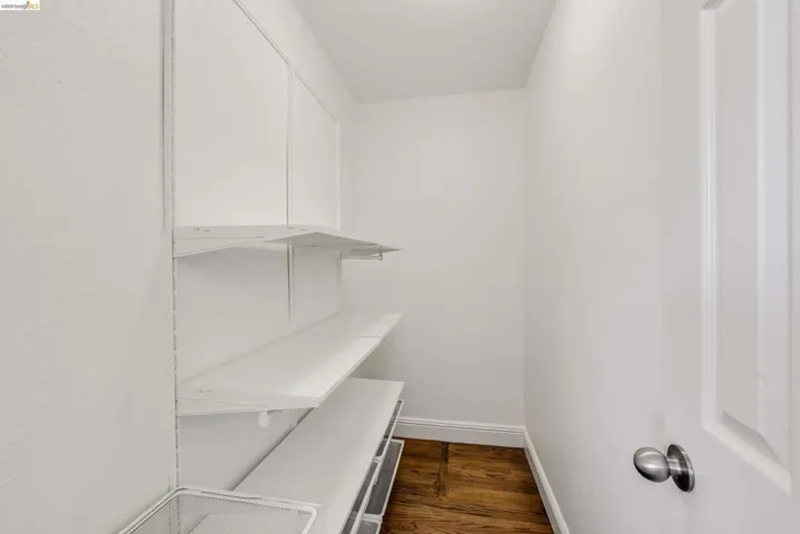 Compact utility space with white walls, wood-finish flooring, and a white paneled door with brushed nickel hardware