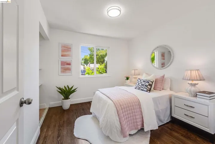 Bright room featuring rich wood-finish flooring, white walls, and a large window providing ample natural light