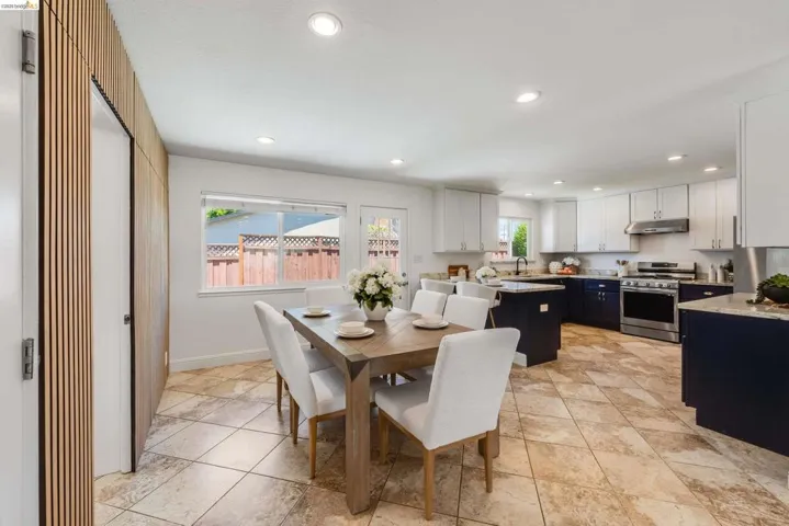 Open-concept kitchen and dining area featuring a two-toned cabinetry design with white upper and dark lower cabinets, a central island with countertop seating, stainless steel appliances, and recessed lighting