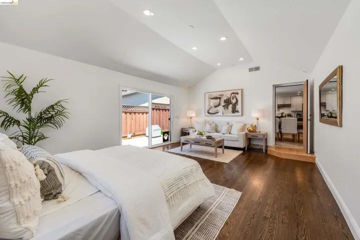 Spacious room featuring vaulted ceilings with recessed lighting, dark wood-finish flooring, and sliding glass doors providing outdoor access