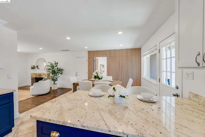 Spacious interior featuring a kitchen with granite countertops and blue base cabinetry, an open-concept dining area with wood slat paneling, and a living area with a stone-clad fireplace and wood-finish flooring