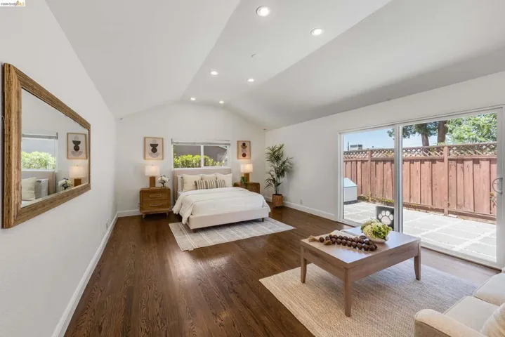 Vaulted ceiling room featuring rich wood-finish flooring, recessed lighting, and a sliding glass door providing direct access to a private paved patio with a wood privacy fence