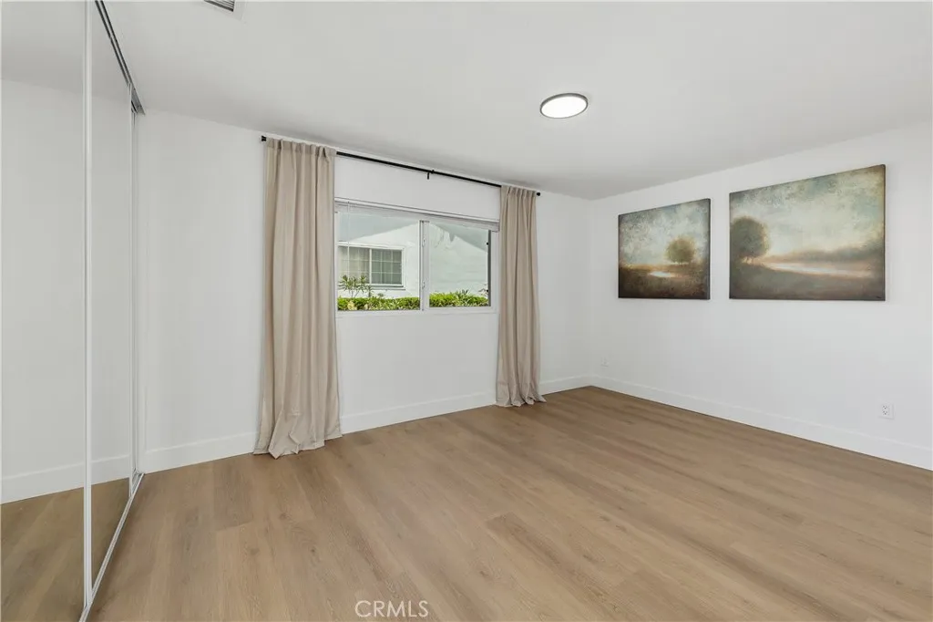 Primary bedroom with ensuite featuring luxury vinyl plank flooring, mirrored closet doors, and stylish black accents in the lighting, door hardware, and curtain rod, complemented by elegant linen curtains and tasteful window treatments for a soft, modern finish.