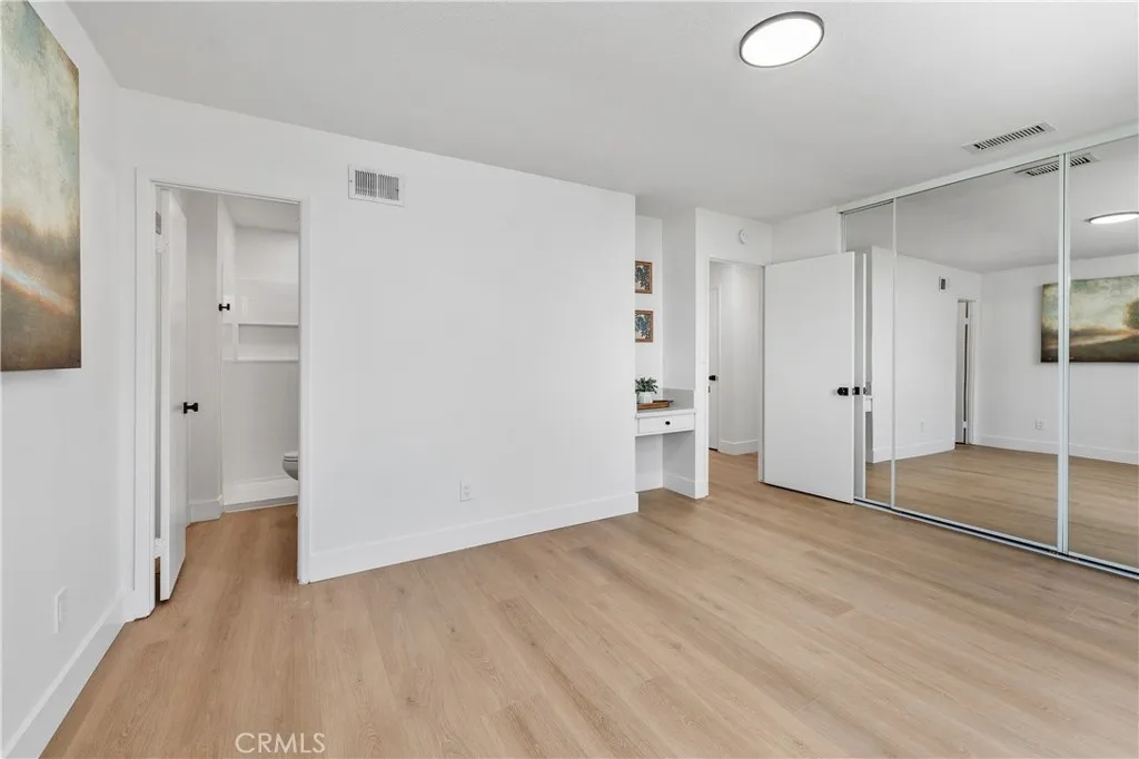 Primary bedroom with ensuite featuring luxury vinyl plank flooring, mirrored closet doors, and stylish black accents in the lighting, door hardware, and curtain rod, creating a cohesive modern design.