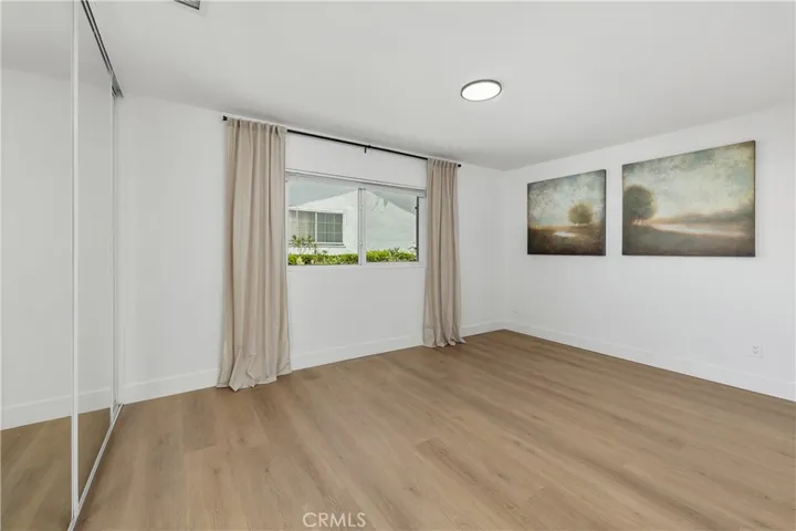 Primary bedroom with ensuite featuring luxury vinyl plank flooring, mirrored closet doors, and stylish black accents in the lighting, door hardware, and curtain rod, complemented by elegant linen curtains and tasteful window treatments for a soft, modern finish.