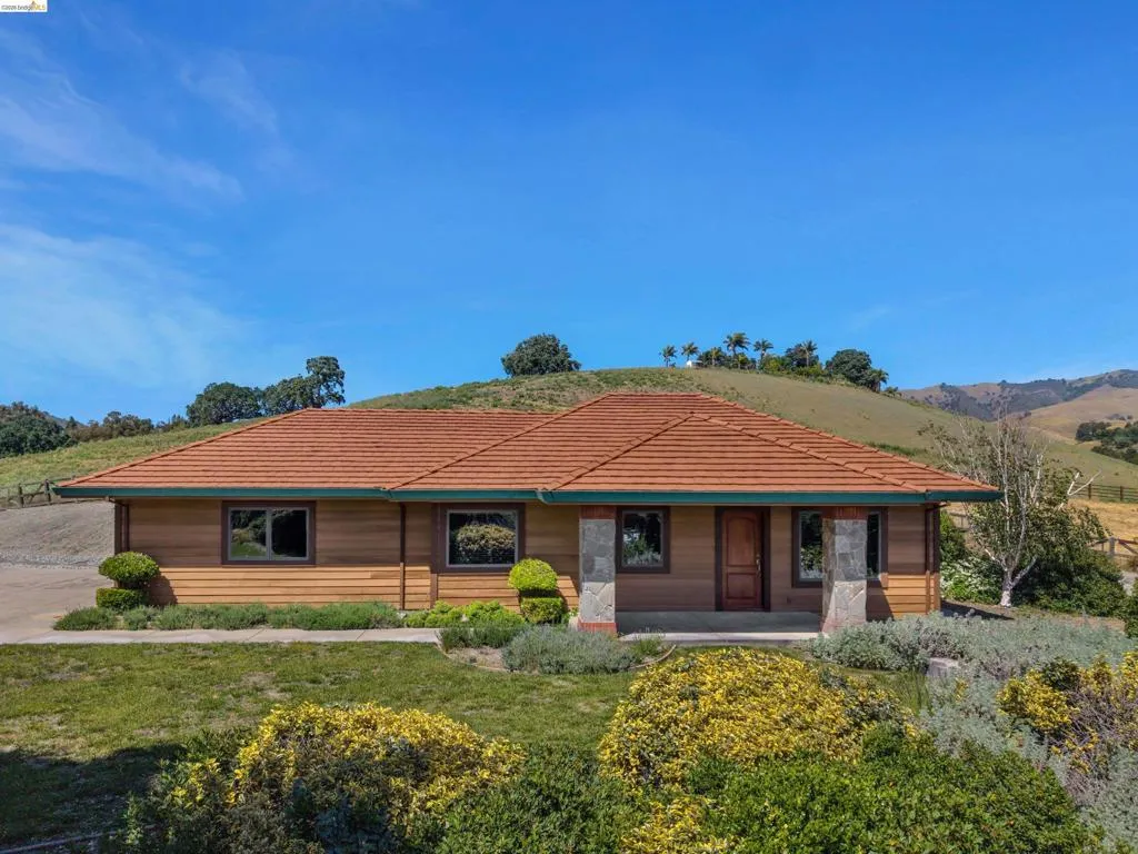 Single-story residence featuring a terracotta-hued tile roof, horizontal wood siding, and stone-clad pillars at the entry