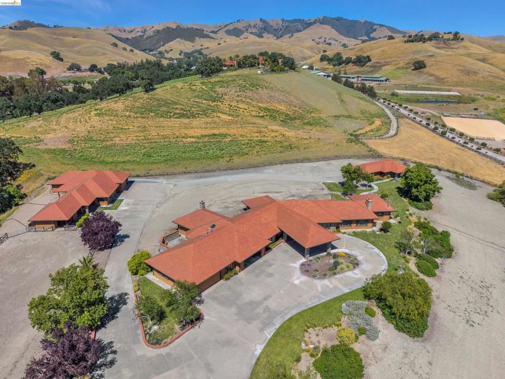 Sprawling property featuring multiple structures with orange tile roofing, extensive concrete paving, and a dedicated riding arena