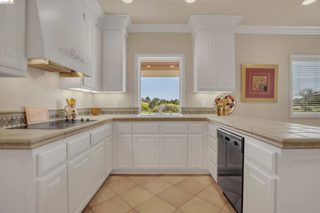U-shaped kitchen featuring white cabinetry with crown molding, tan tile countertops, and a patterned tile backsplash