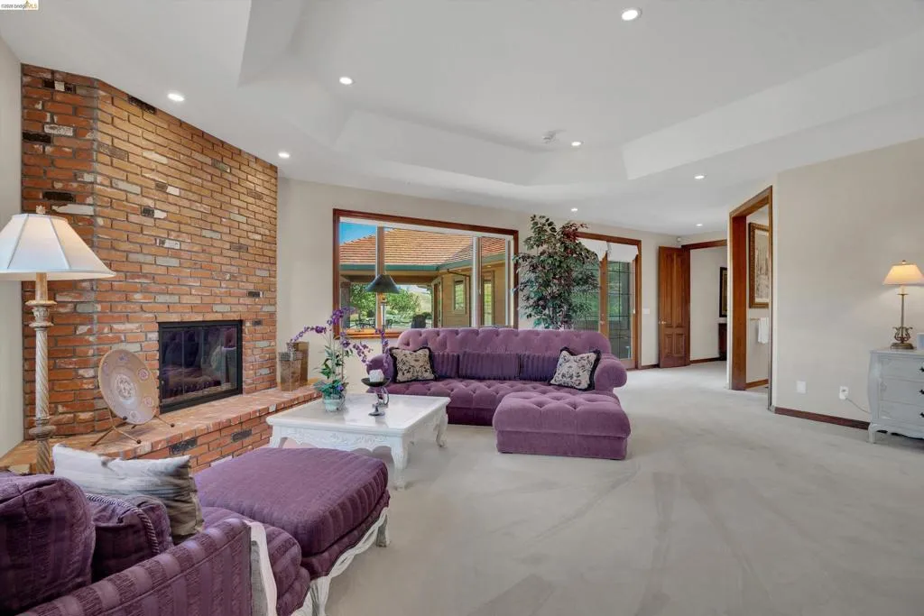 Spacious interior featuring a large brick fireplace, tray ceiling, recessed lighting, and a wide window with exterior views