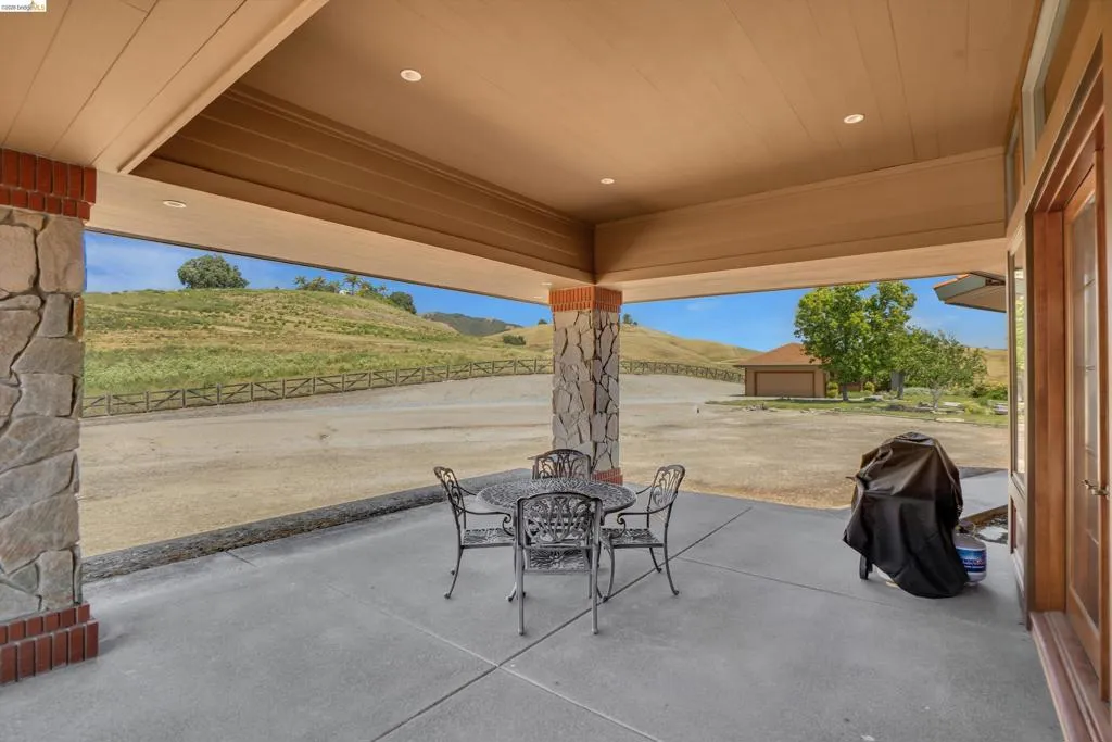 Covered patio featuring stone veneer columns with brick bases, recessed lighting, and a wood-finish ceiling