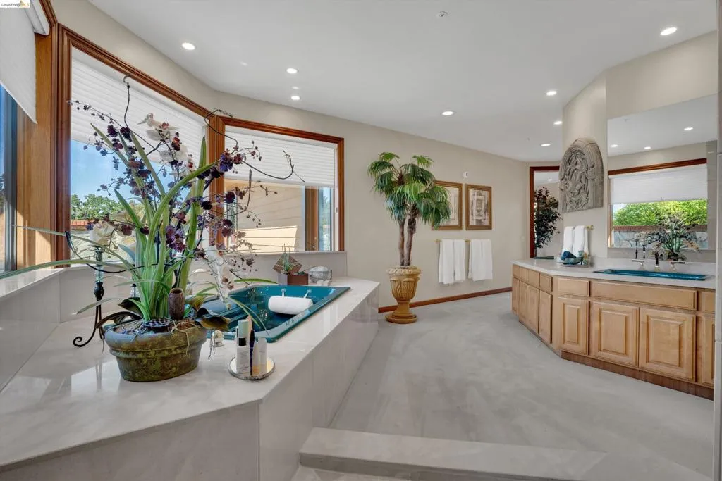 Expansive bathroom featuring a built-in soaking tub, large windows with privacy blinds, dual vanity with undermount sinks, and light wood cabinetry
