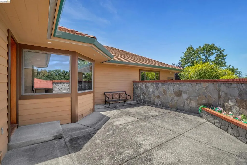 Exterior featuring tan siding with dark brown trim, a terracotta-style roof, and a stone retaining wall