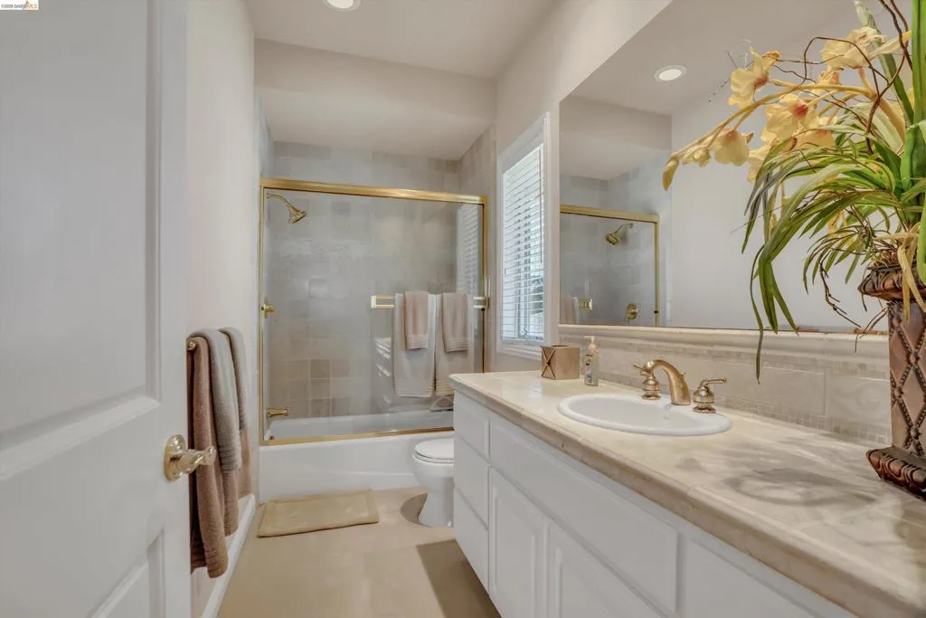 Bathroom featuring a single vanity with a light-toned countertop and integrated sink, gold-toned fixtures, a mirrored wall, and recessed lighting