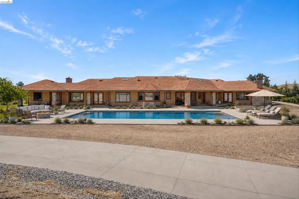 Expansive rear exterior featuring a large swimming pool, surrounding concrete patio, and mature landscaping