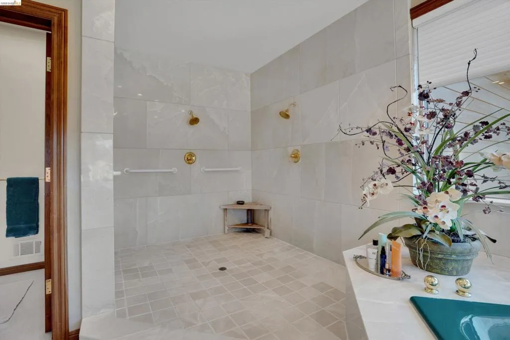 Expansive walk-in shower featuring large format wall tiles, dual brass shower heads, and an integrated corner bench