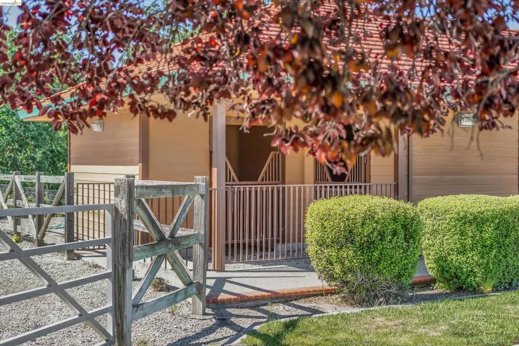 Equestrian facility featuring a covered structure with multiple stalls, a wood-slat exterior, and a red-tile roof