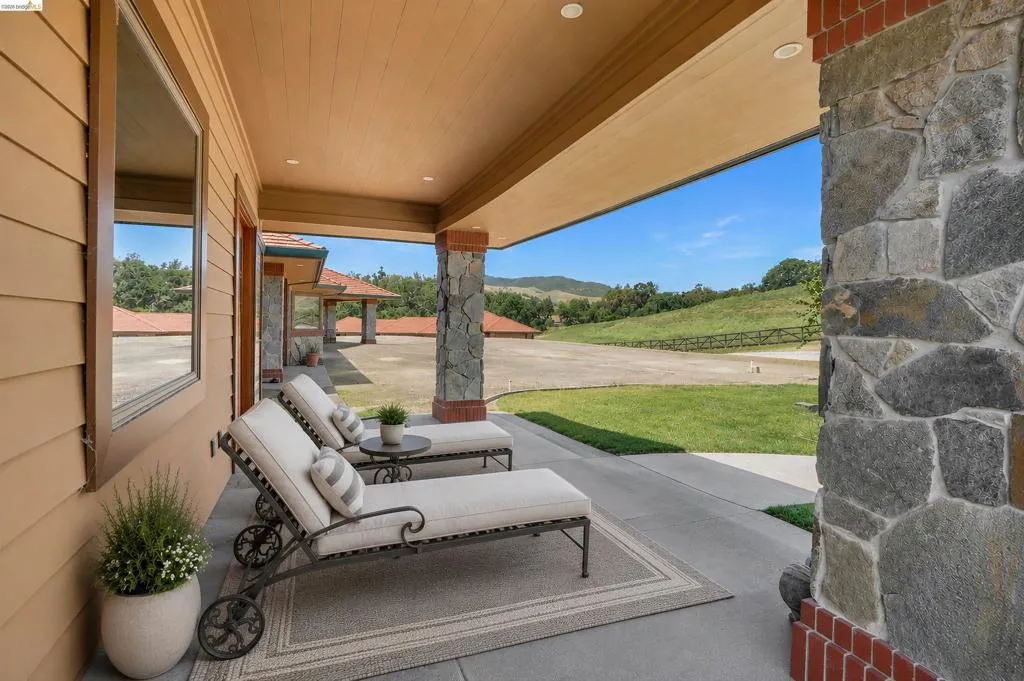 Expansive covered patio featuring stone columns with brick accents, recessed lighting, and a concrete floor