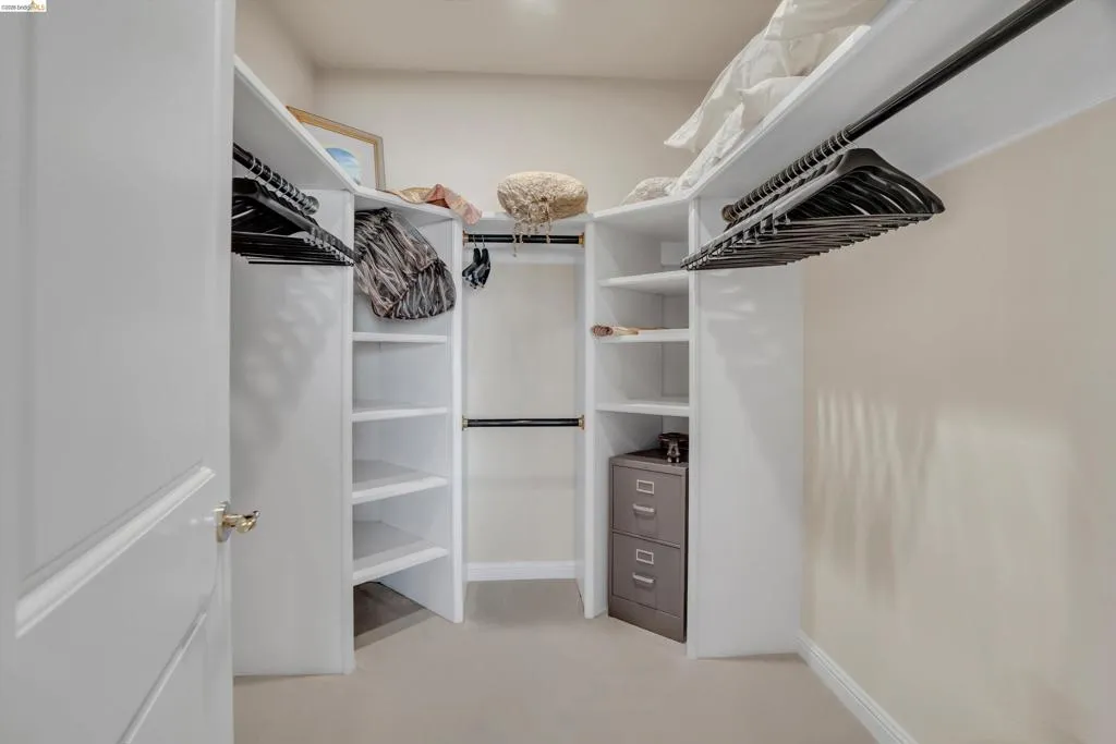 Walk-in closet featuring built-in white shelving, multiple hanging rods, corner storage, and neutral wall paint