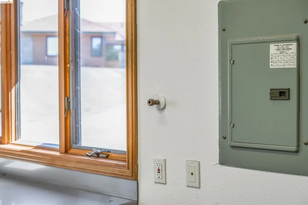 Light-filled interior space featuring a multi-pane wood-framed window, white painted walls, a gray electrical panel, and a wall-mounted gas line connection