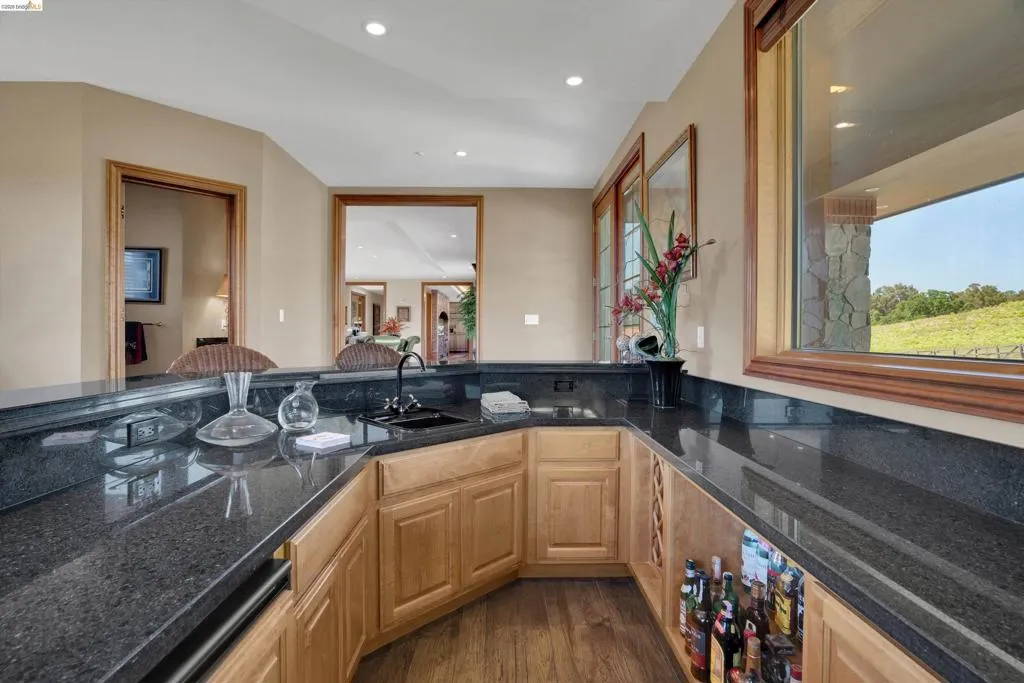 Wet bar featuring dark granite countertops, an undermount sink, recessed lighting, wood-finish flooring, and natural wood cabinetry