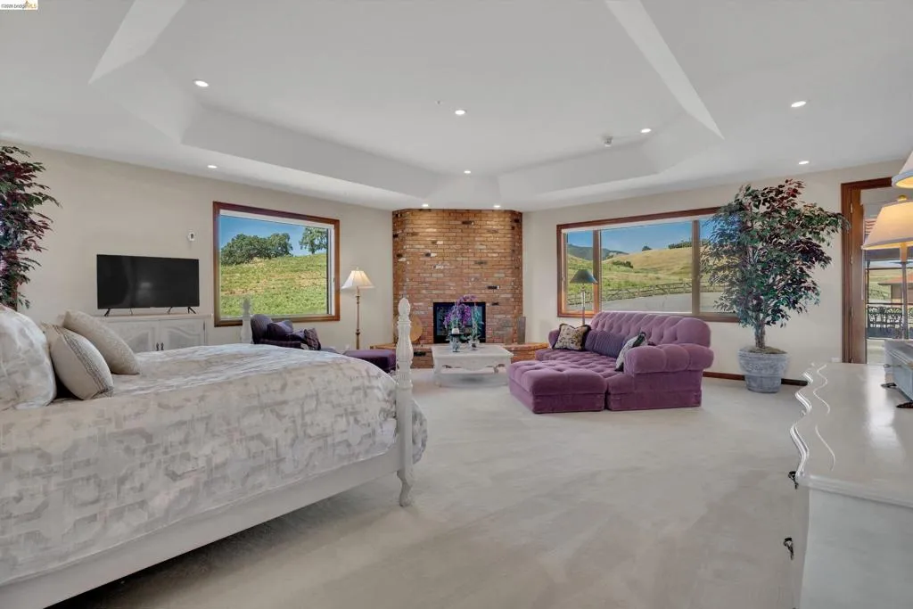 Expansive room featuring a tray ceiling with recessed lighting, a corner brick fireplace, and multiple picture windows