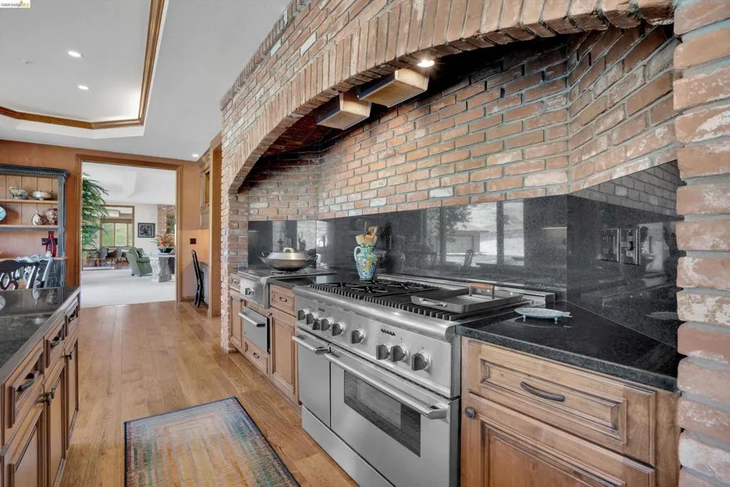 Kitchen featuring a large stainless steel range with a griddle, black countertops, wood-finish flooring, and exposed brick archway